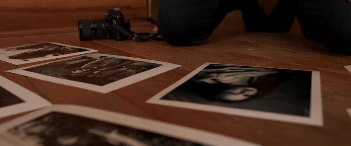 Photographer kneels on wooden floor examining black and white photographs