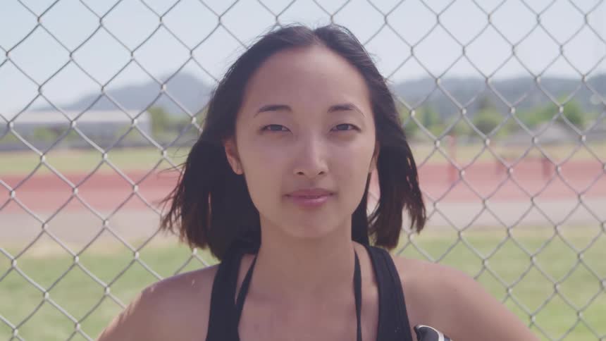 An asian female standing outside smiling near a fence