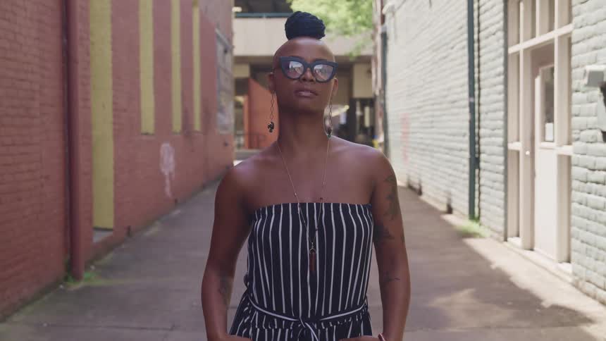 A black woman stands in an alley on a sunny day posing