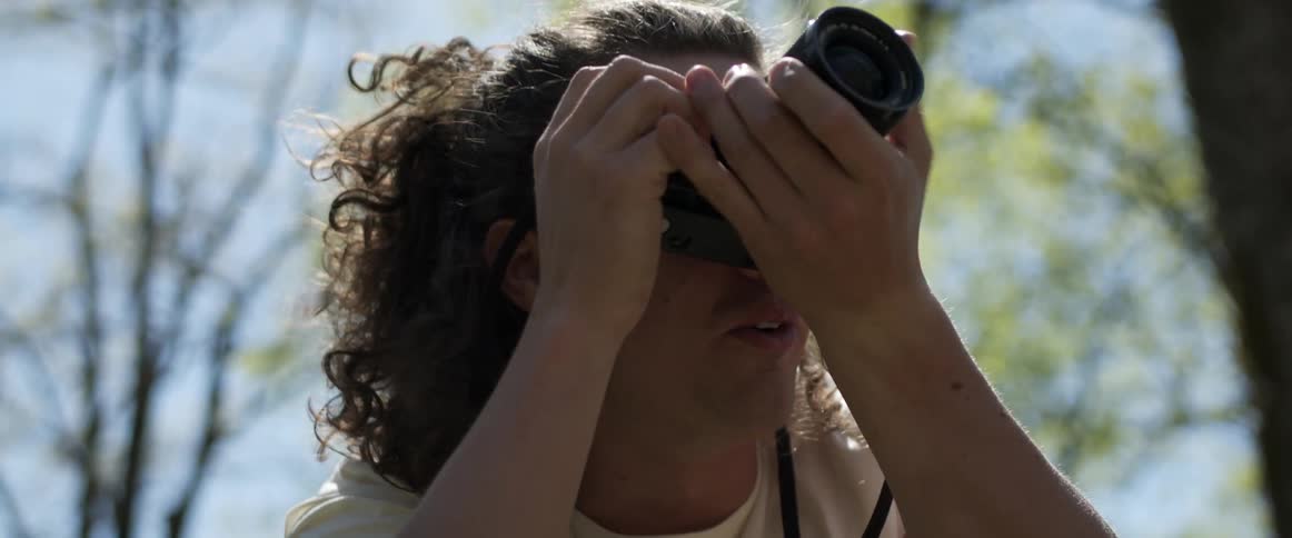 A male photographer taking a photo outside near trees on a summer day