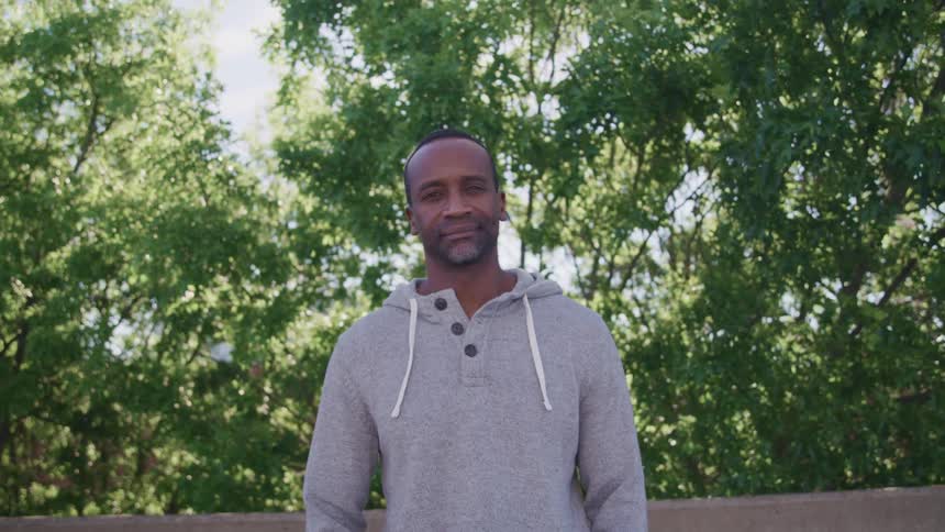 A man stands outdoors and looks confidently towards the camera while posing for a portrait