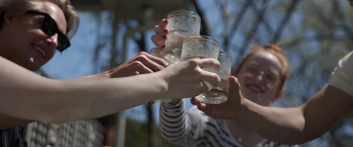Friends sitting outdoors near fence clink glasses