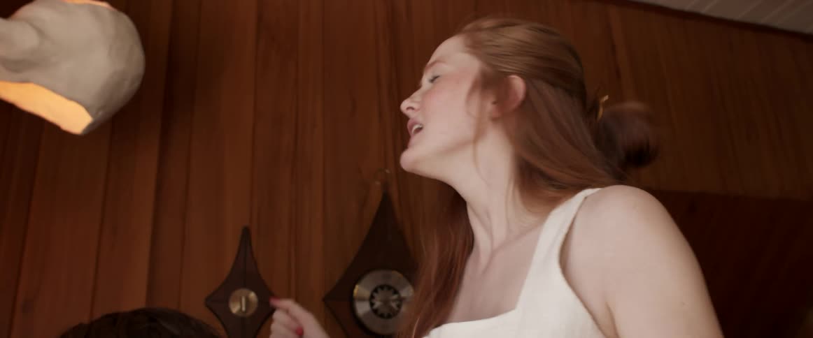 A woman singing and dancing behind a man sitting down playing an instrument indoors