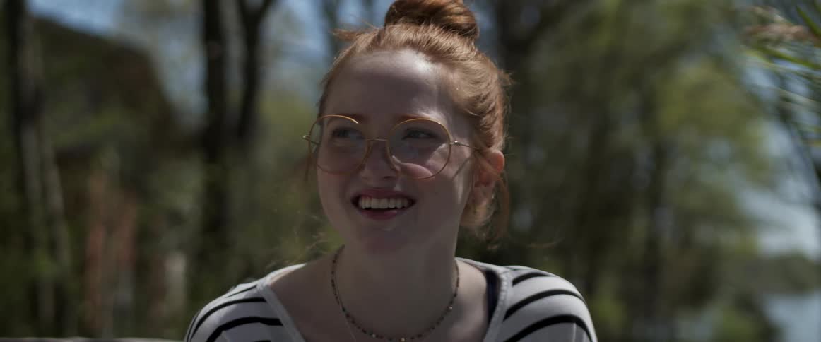 A woman with glasses with trees the sky and clouds in the background