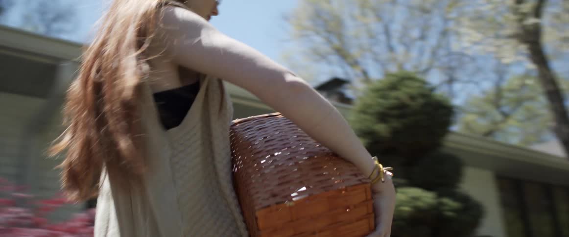 A teenager takes a basket out of her vehicle and starts to carry it to a house