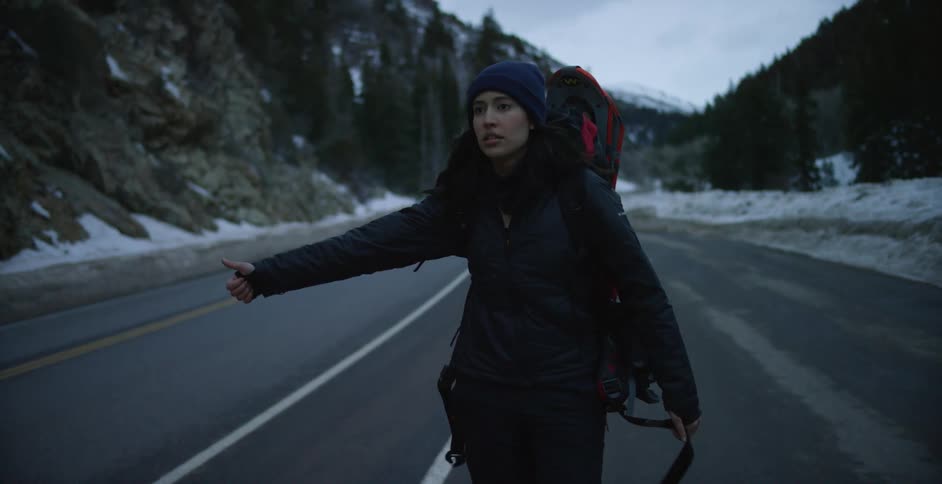 A woman is hitchhiking on the snow lined road