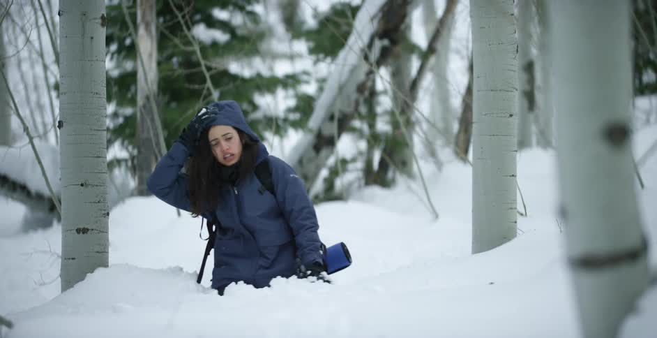 Woman trudges through snow covered forest collapsing to knees