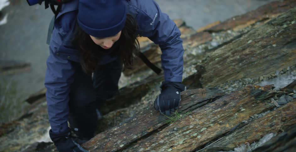 Woman wearing a backpack climbingover piled logs outdoors at winter