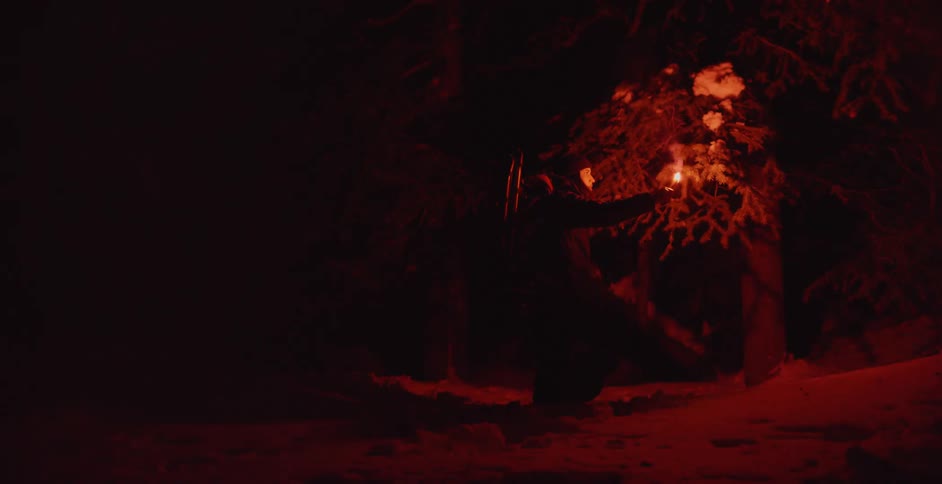 A woman using a flare to look around a forest at night