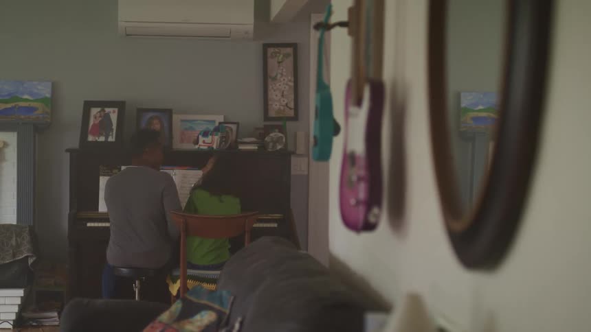 A dad sitting next to his daughter as they play the piano together