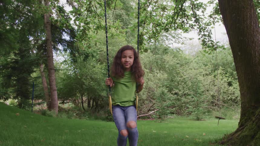 A girl sitting on a swing with trees the sky and clouds in the background