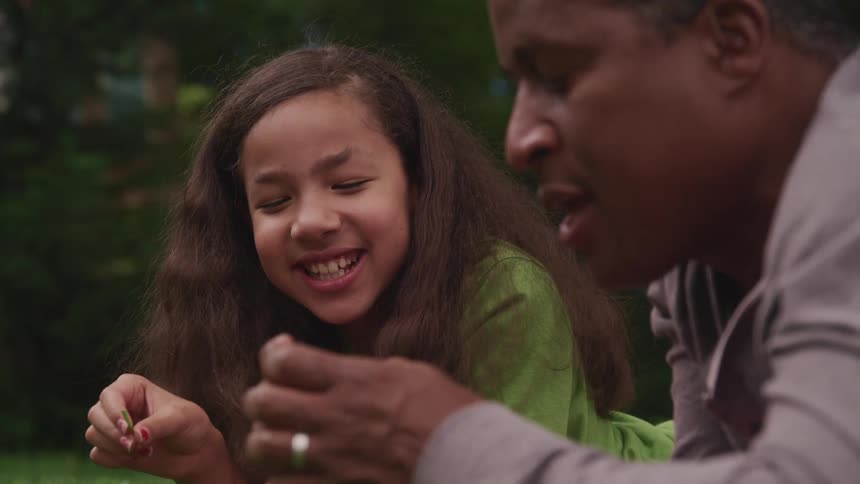 Father and daughter laugh lying down on ground outdoors