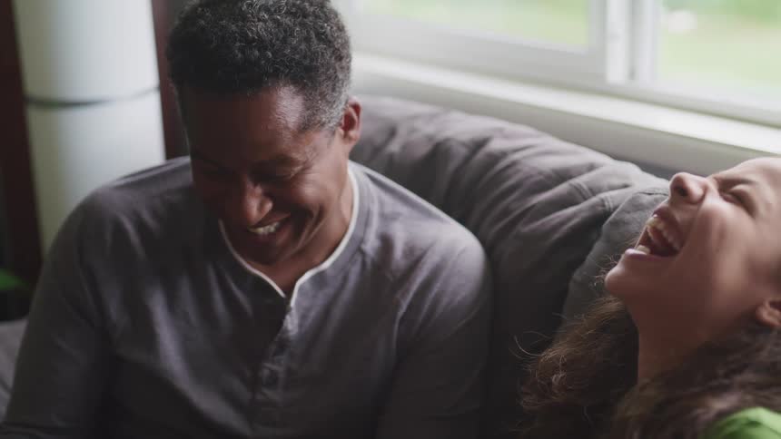 A father and daughter laughing on a couch
