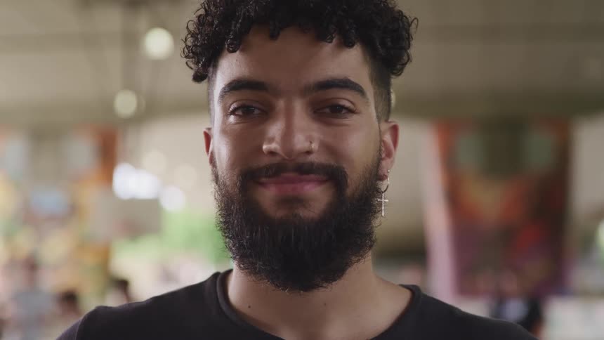 Bearded young man standing in a public space looking at the camera