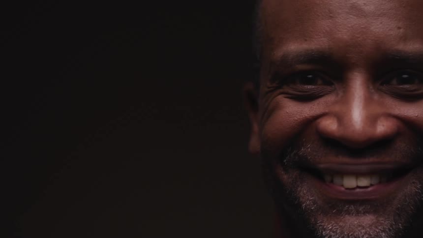 A man in a room smiling with a wall in the background