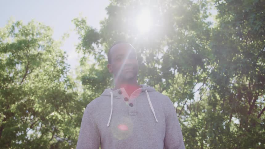 Sun glares down through trees onto man standing and smiling