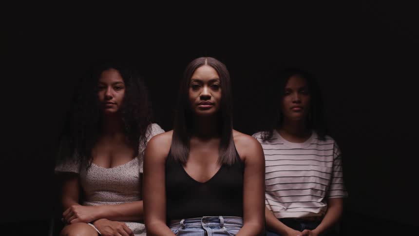 Three black women lift their heads and look straight ahead against a black background