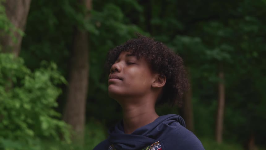 Man stands outdoors in forest closing his eyes to breath the air