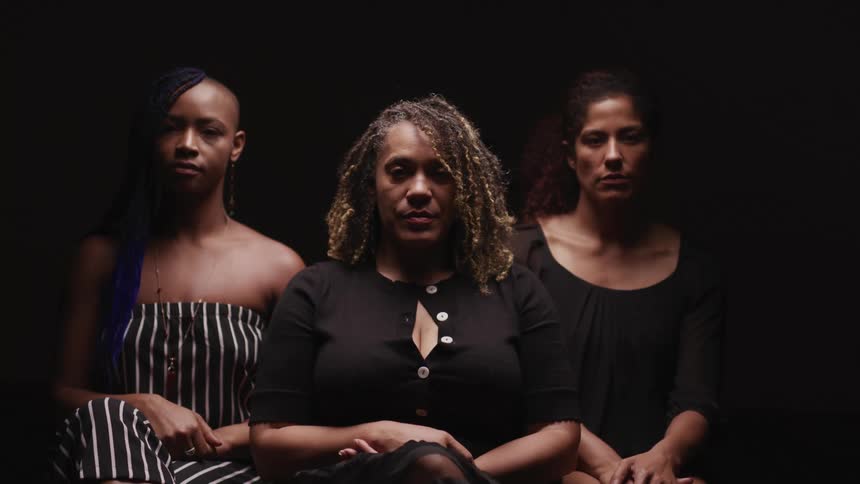 Three woman standing together all turn their heads to look at the camera