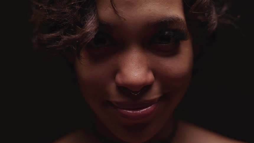 Close up of a smiling womans face looking at the camera in a dark room