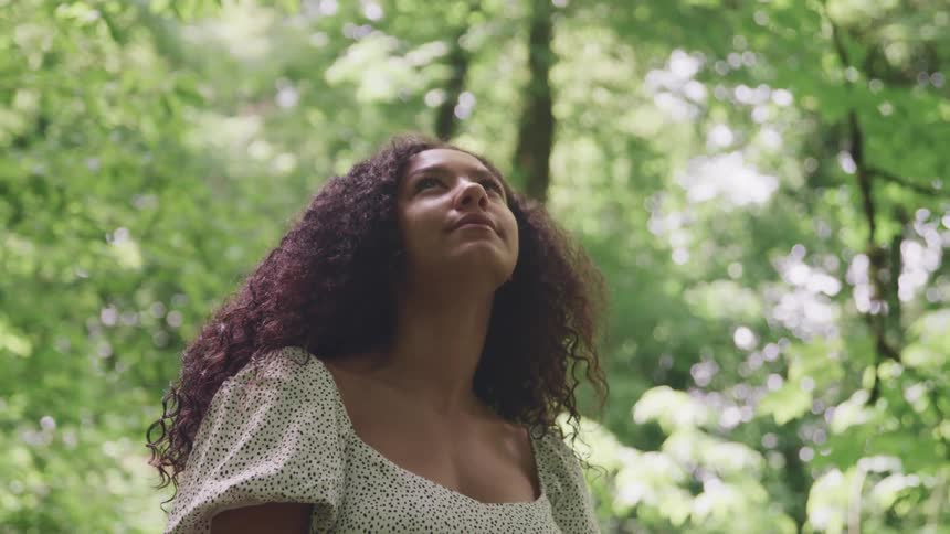 Young woman with curly long hair standing in the forest looking up