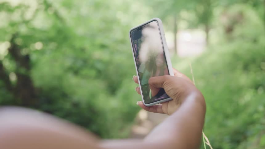 Three smiling women standing in woods take group selfie using mobile phone