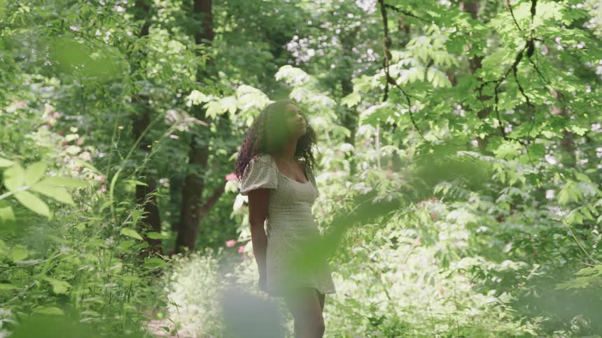 Young woman wearing a white dress standing in the forest looking up