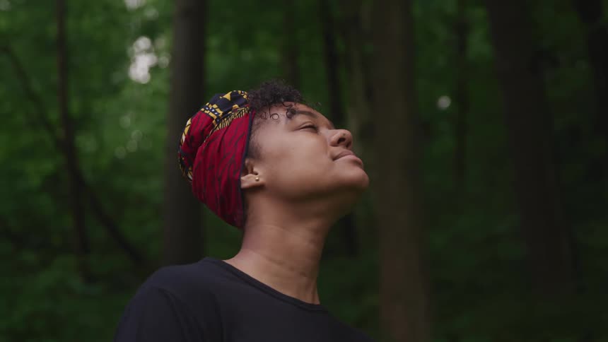 A woman looking up while standing alone in a forest in summer