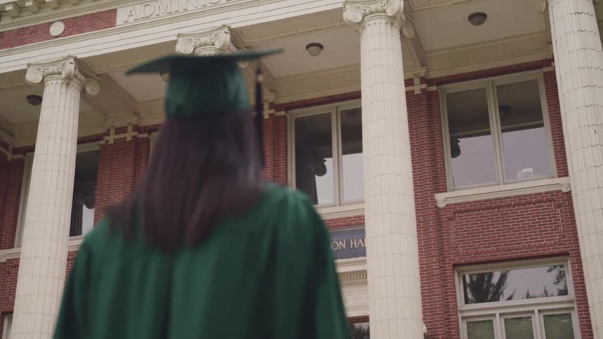 A woman with a graduation cap and gown with a building with pillars in the background