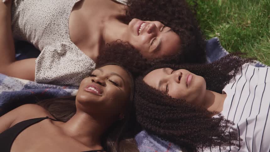 Three women laying on a blanket on grass