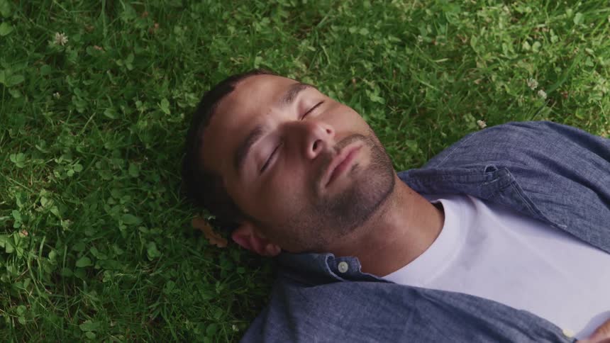 A man sleeps on his back in the grass during the day