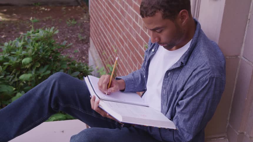 A man sitting outside writing in a book