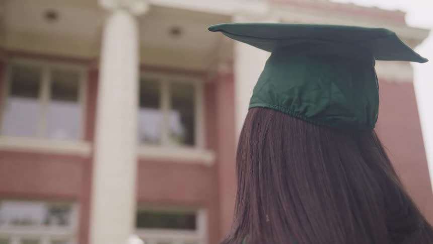 A woman standing with a graduation cap with a building the sky and clouds in the background