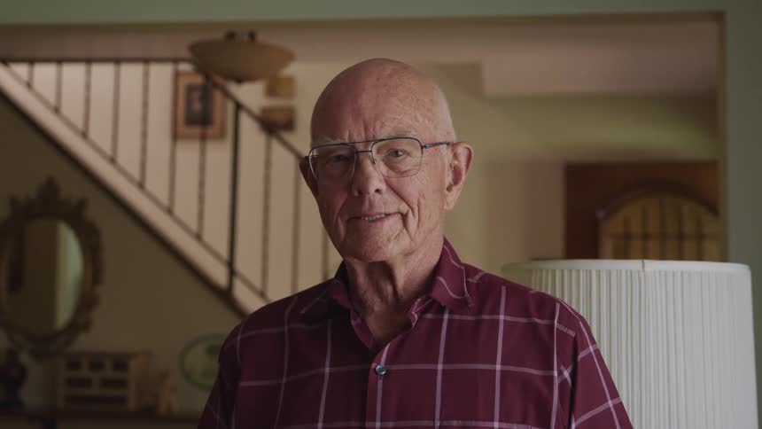 Elderly man standing in the living room at home looking at the camera