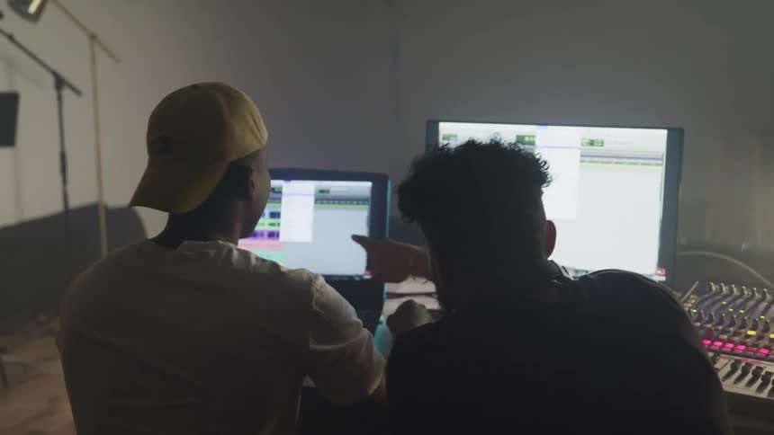Two men look over a music creation program on a laptop as they make music