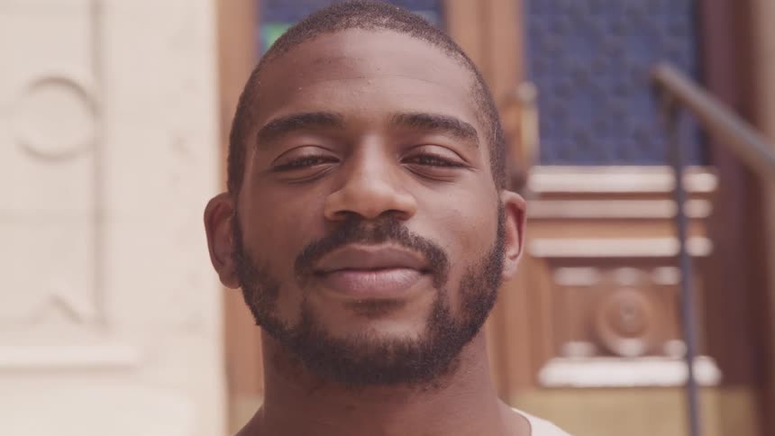 A man staring with a building a banister and doors in the background