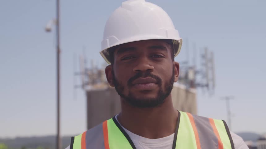 Construction worker wearing a white hardhat turns to look at the camera