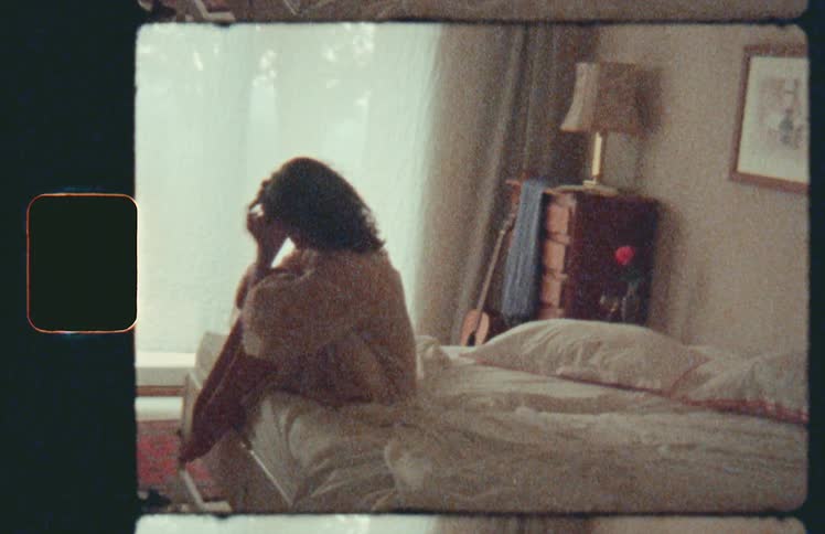 Female sitting on bed in bedroom with her knees against her check drops her face into her knees as she is feeling upset