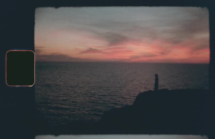 A woman stands on the edge of a cliff overlooking the ocean