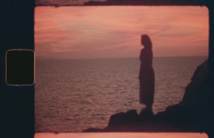 Silhouette of woman standing on rock looking at the ocean at sunset