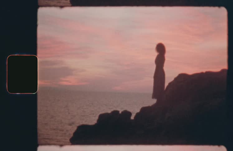 Woman standing on rocks silhouetted against sunset and ocean