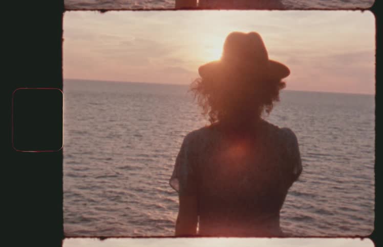 Vintage footage of young woman silhouetted against sunset over ocean