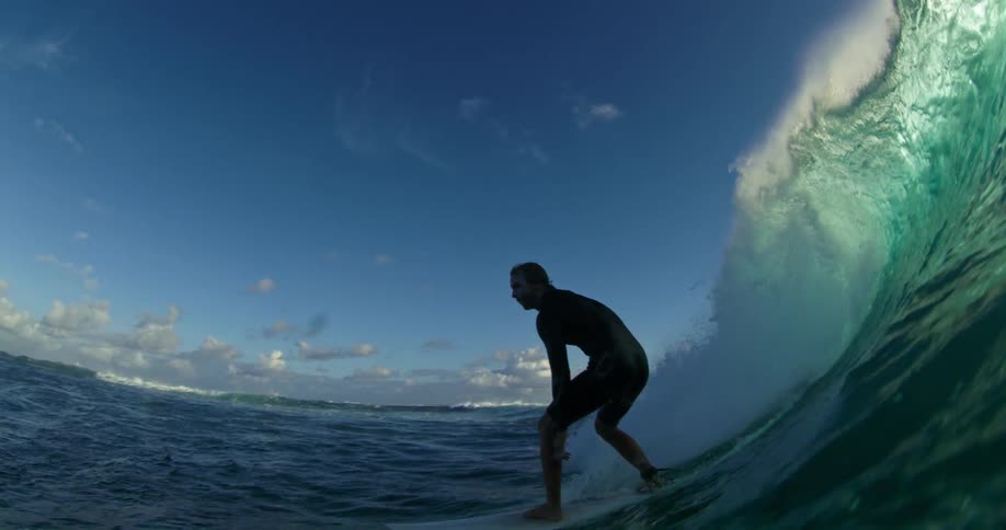 A man rides a surfboard on a wind wave that blocks out the sun in the ocean