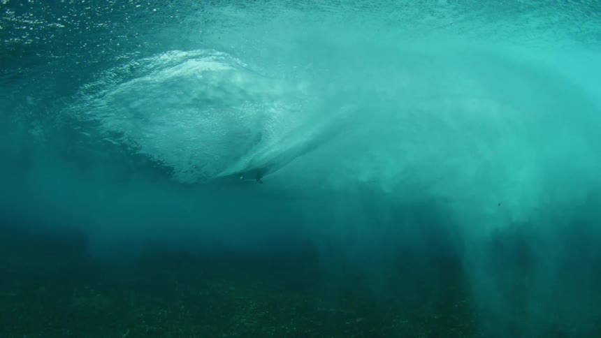 A surfer riding a wave is visible on the surface from underwater
