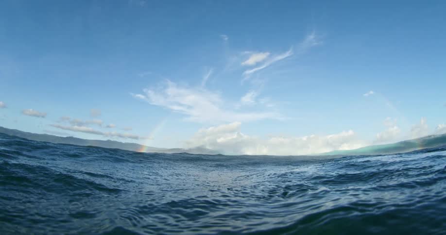 Water ripples and waves under a cloudy sky with a rainbow