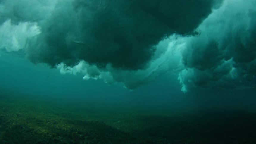 A sea wave sends clouds of bubbles reaching towards the sea floor