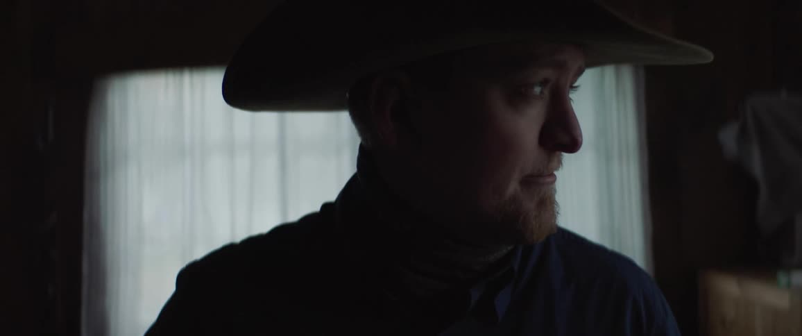 A man adjusting his cowboy hat then looking off to the side