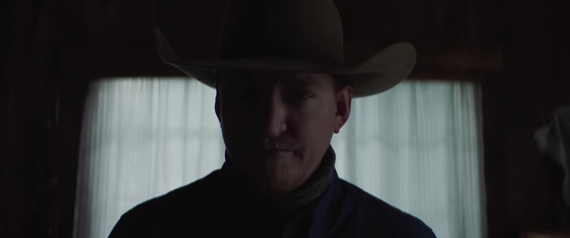 A man poses in a cowboy hat in front ofa large window