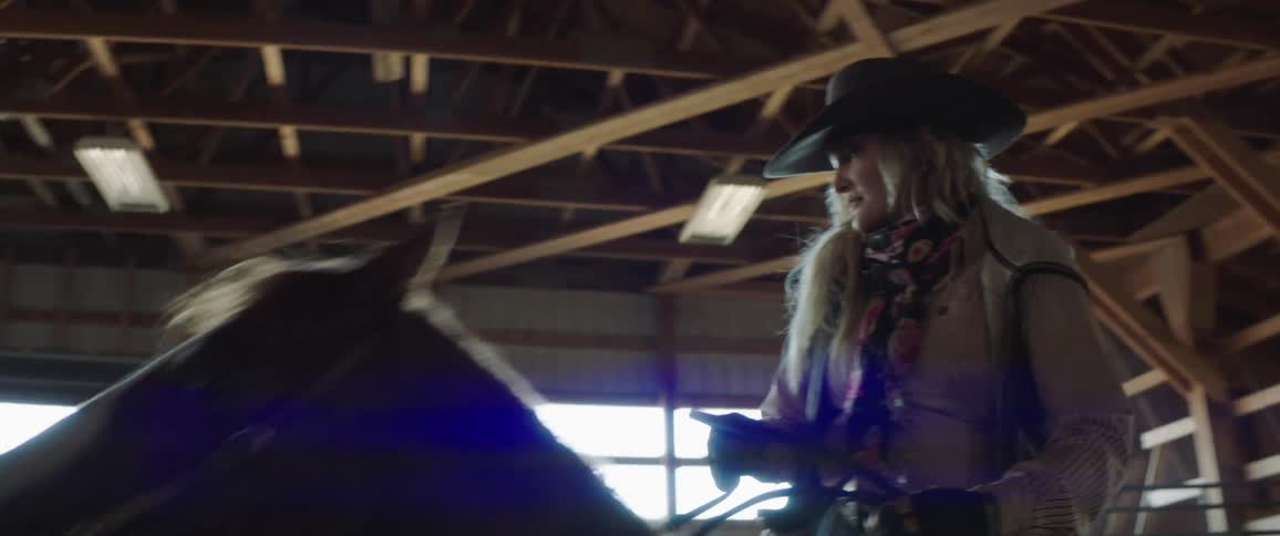 A woman rides a horse inside a stable during the day