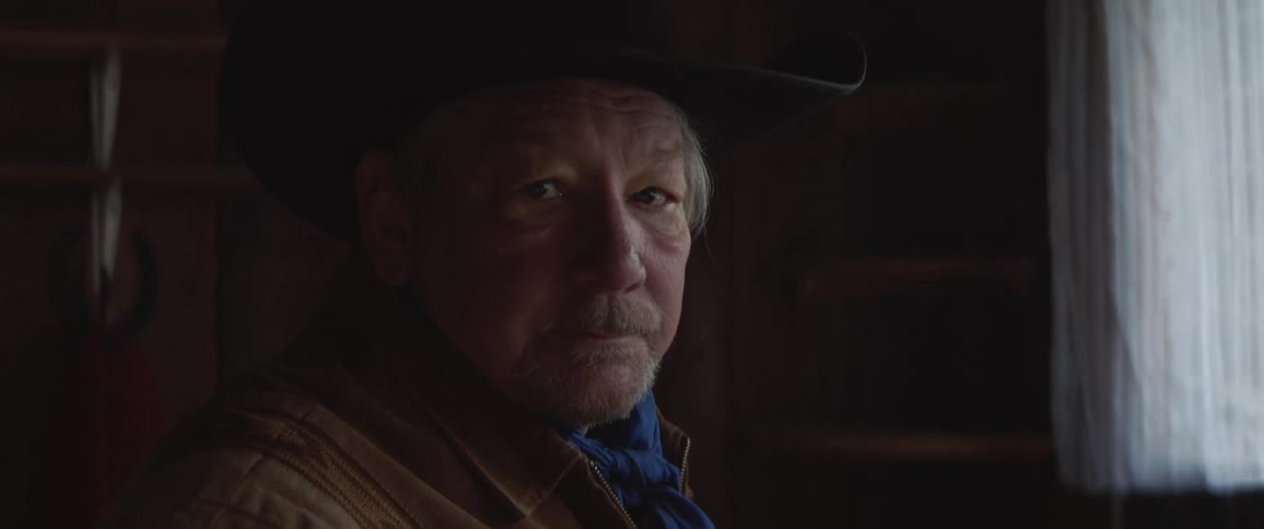 Elderly man in cowboy hat and bandana looks into camera
